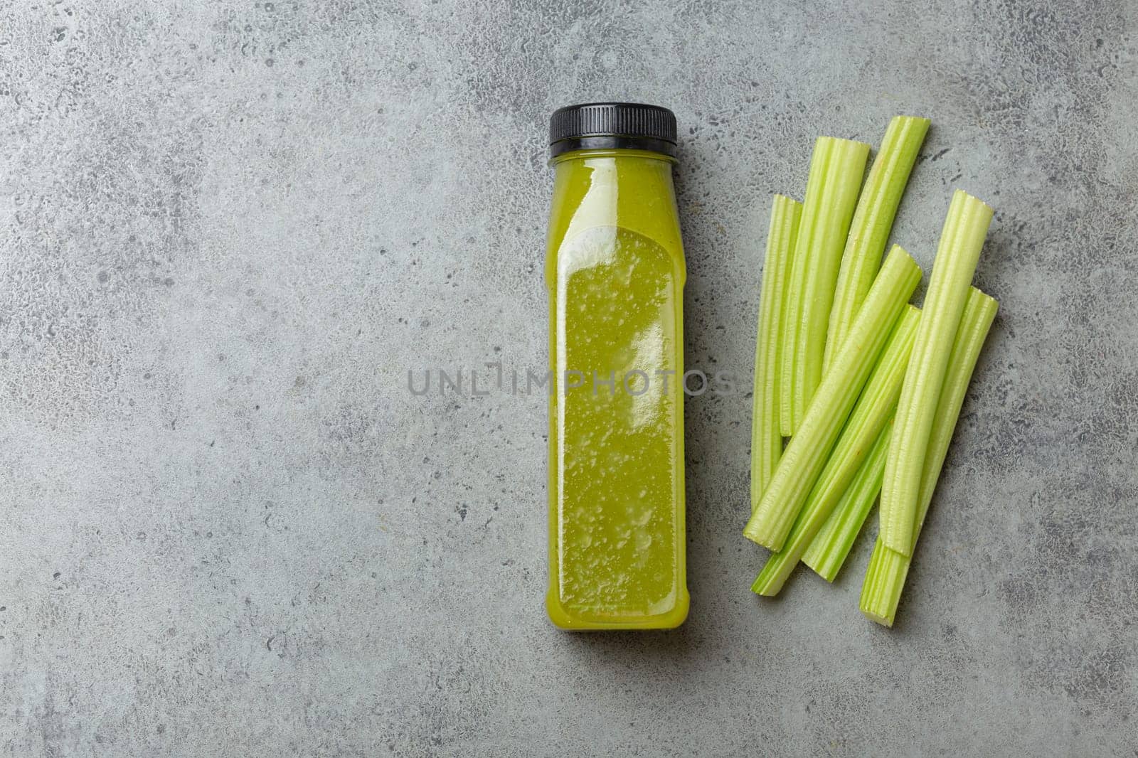 Bottle of green celery smoothie with fresh celery sticks on gray concrete background top view. Diet beverage, healthy nutrition, detox concept by its_al_dente