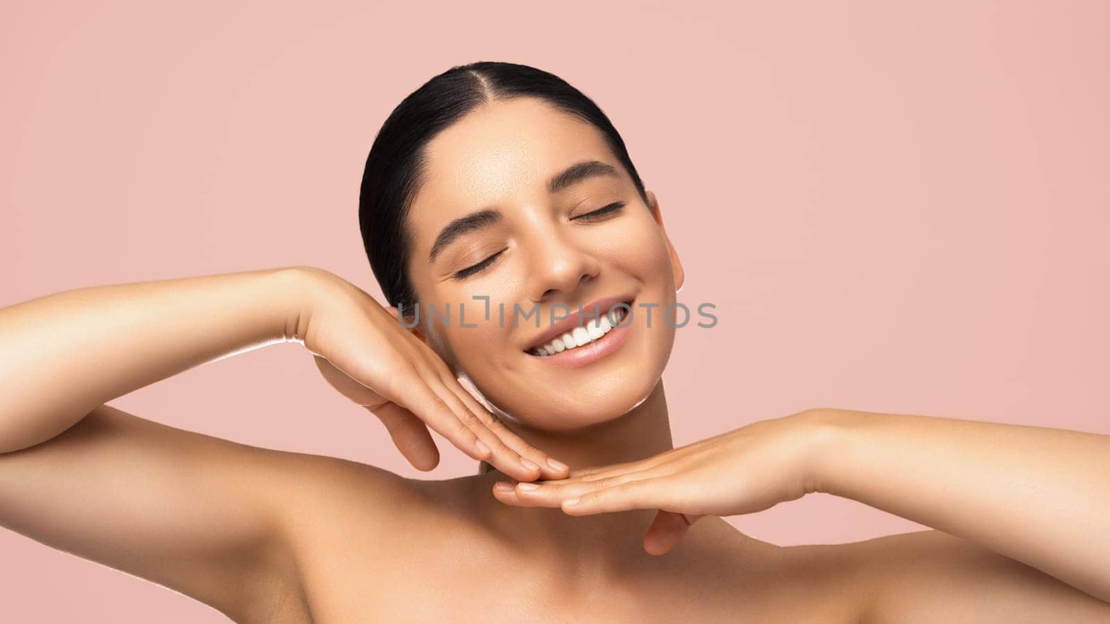 Beauty portrait of cheerful beautiful woman smiling with eyes closed tilted head and gentle hands next to face.