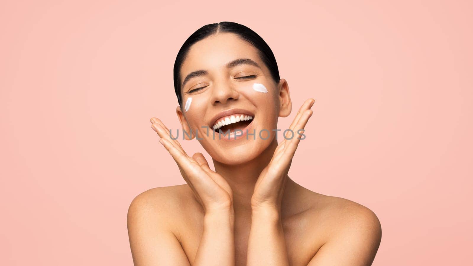 Face skincare. Beautiful multi-ethnic woman with cheerful smile applying moisturizer on face. Beauty portrait by AndreiDavid