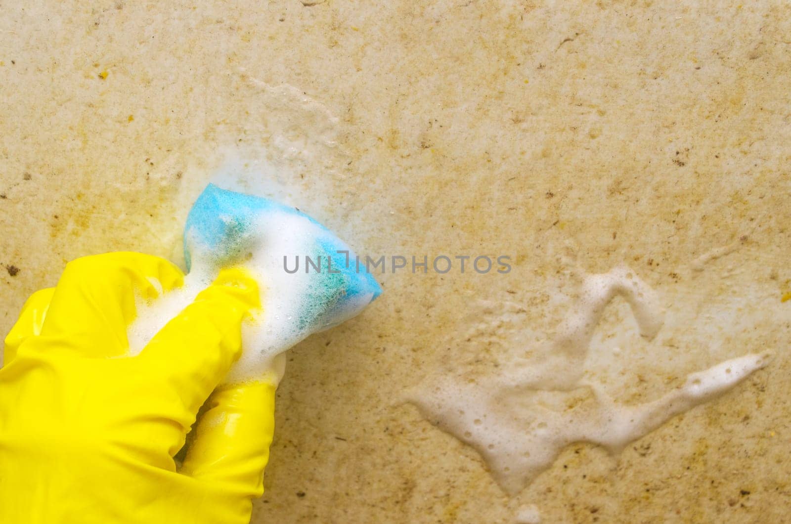 A man in a yellow protective glove is washing a very dirty bath with a blue sponge. Regular cleaning in the bathroom.