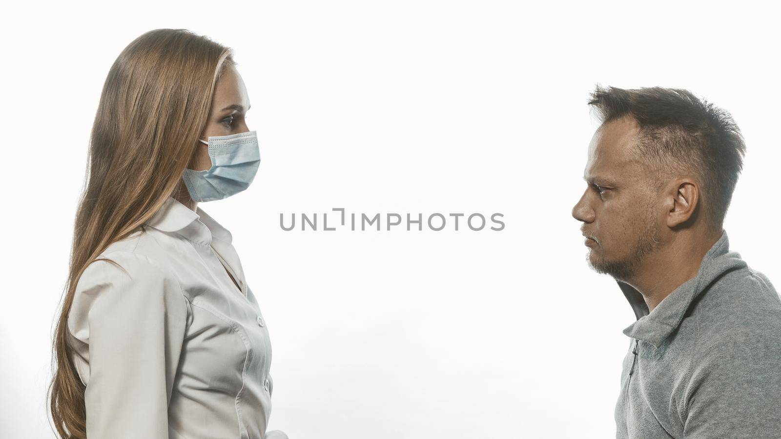 Medic looking at male patient who came for tests wearing a medical face mask. Sad man looking at her with sad eyes. Isolated on white background. Tinted image by LipikStockMedia