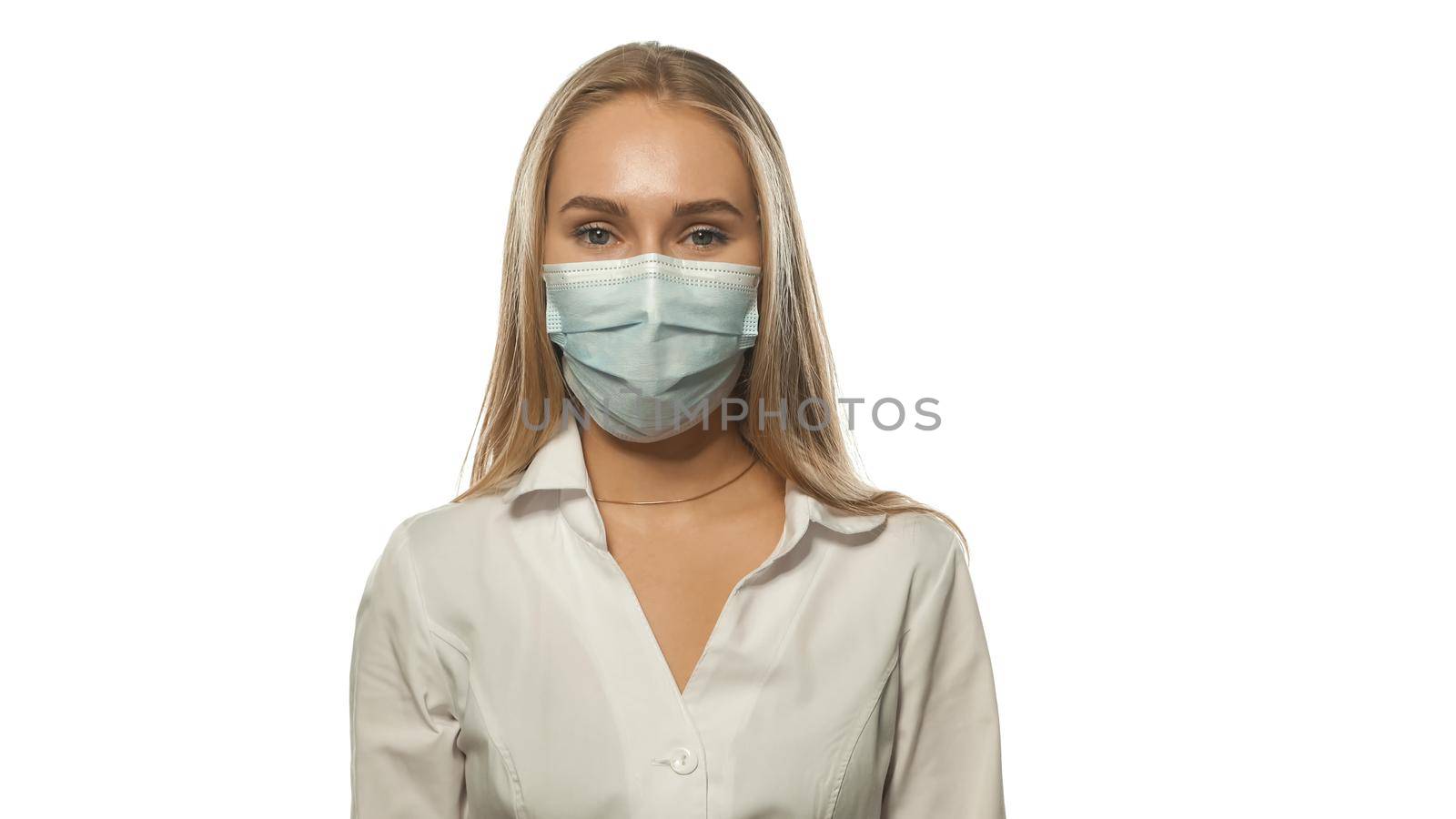 Charing blond haired nurse in a medical mask and white uniform looking at the camera. Isolated on white background by LipikStockMedia