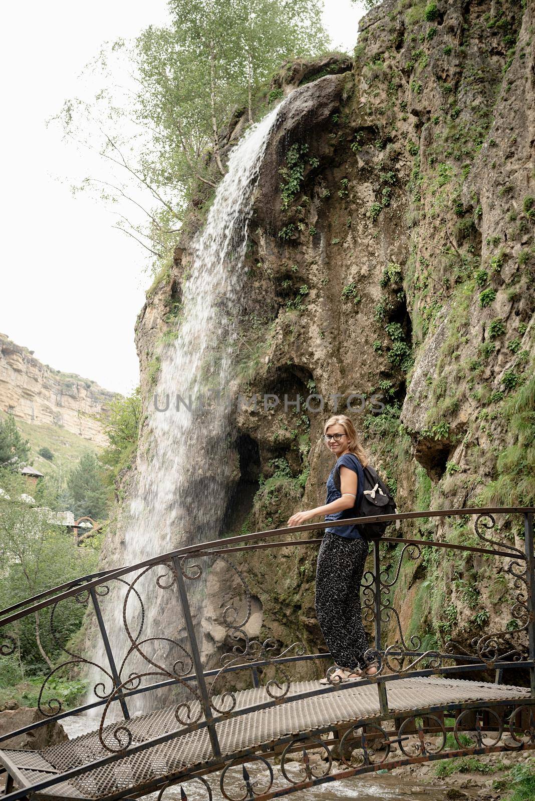 Woman standing on bridge looking at the Beautiful mountain waterfall by Desperada