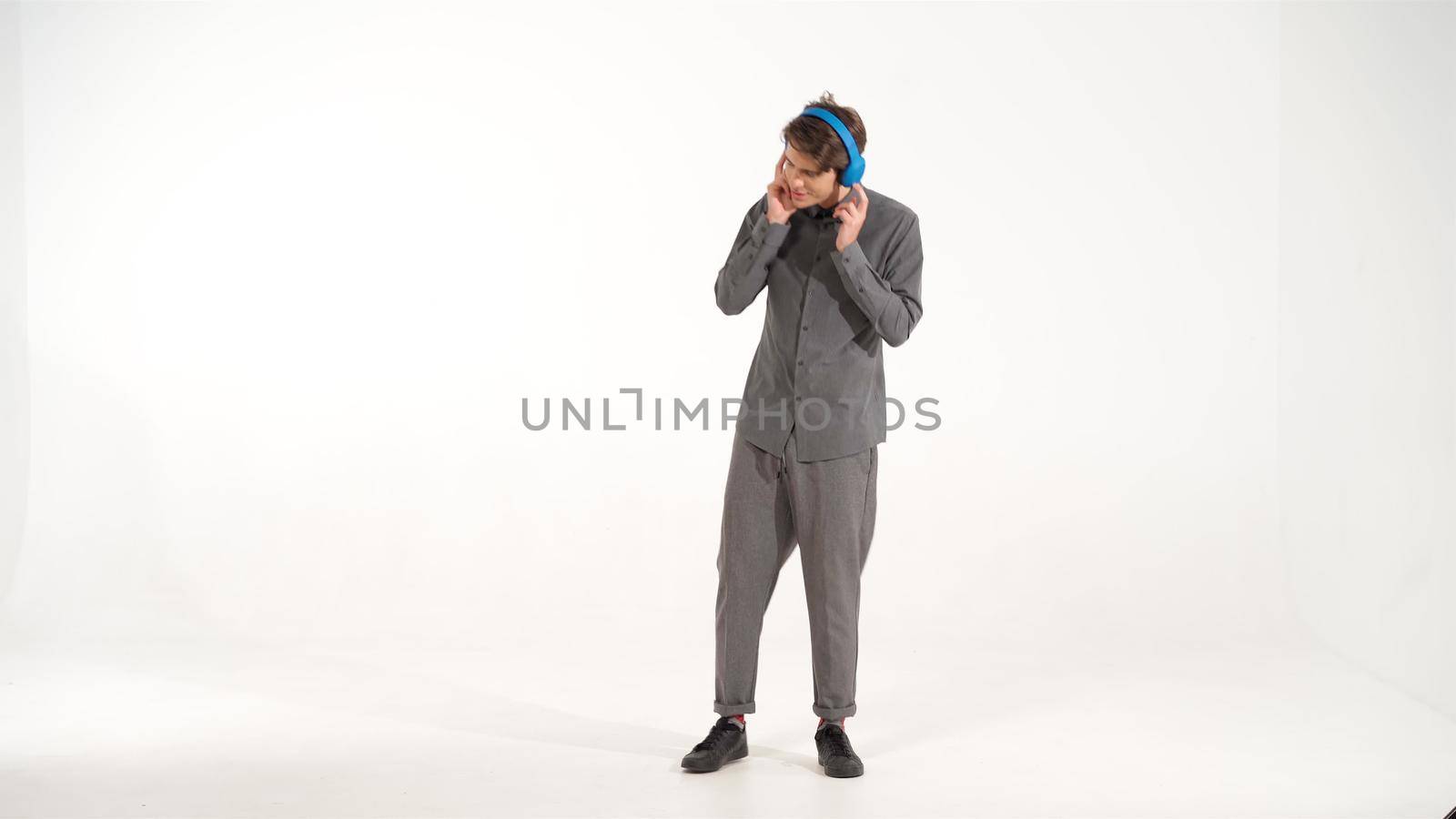 Full length dancing young man in grey sports outfit listening music wearing blue wireless headphones. Funny dancing young guy listen to his favourite track or song. 4K footage by LipikStockMedia