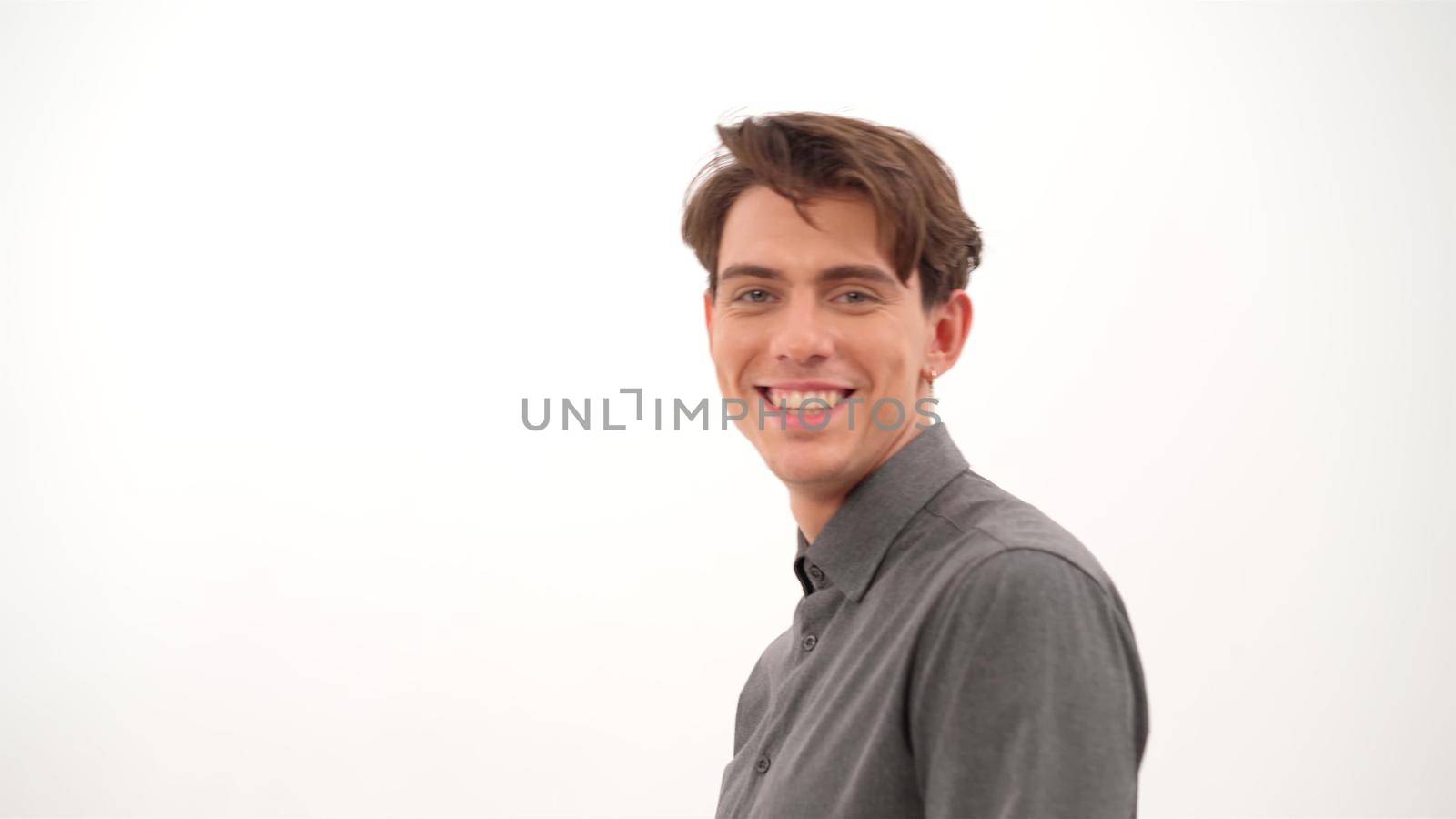 Smiling handsome young man turn fixing his hair and looking at camera wearing grey shirt isolated on white background. 4K video by LipikStockMedia