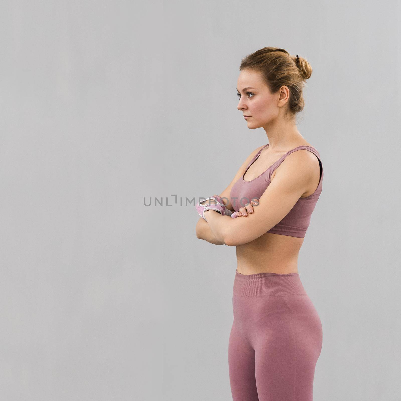 Standing with folded arms fitness girl wearing pink outfit exercising at home. Sport and recreation concept. Pensive girl is enjoying with her training process working hard. Square image by LipikStockMedia