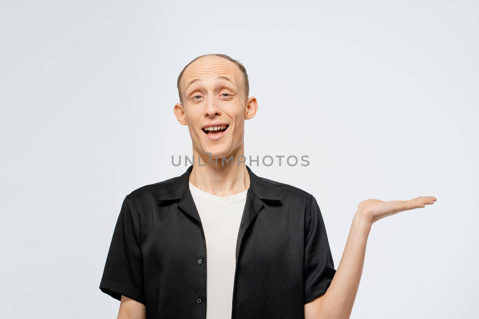 Holding a banner on a left hand free place for your text young bald man in black shirt with white t-shirt under. Happy young man showing copy space for your product isolated on white background.