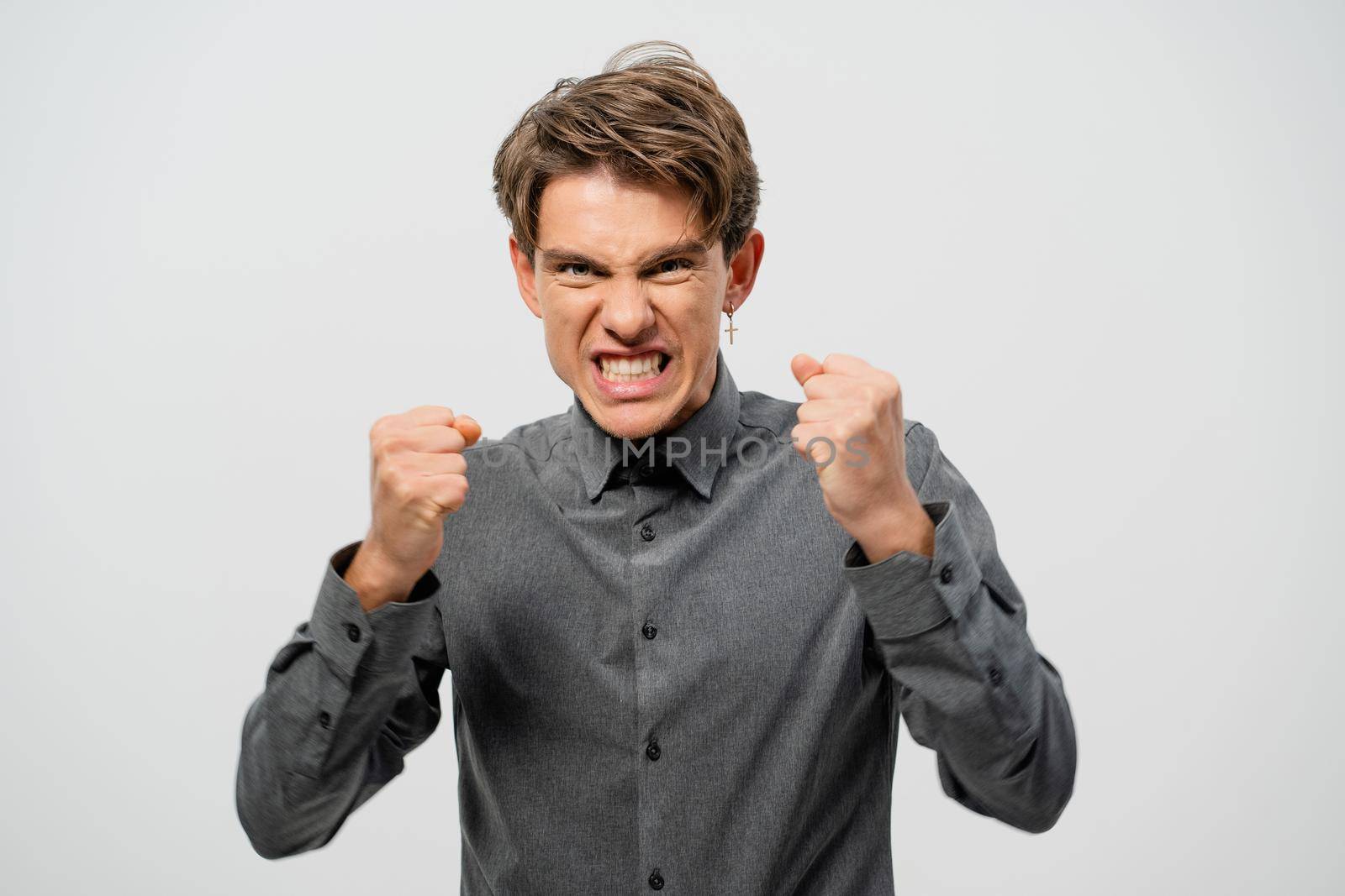 Ready to fight young man defending himself hands in fists in grey shirt with. Angry young adult man showing he is ready for fight isolated on white background.