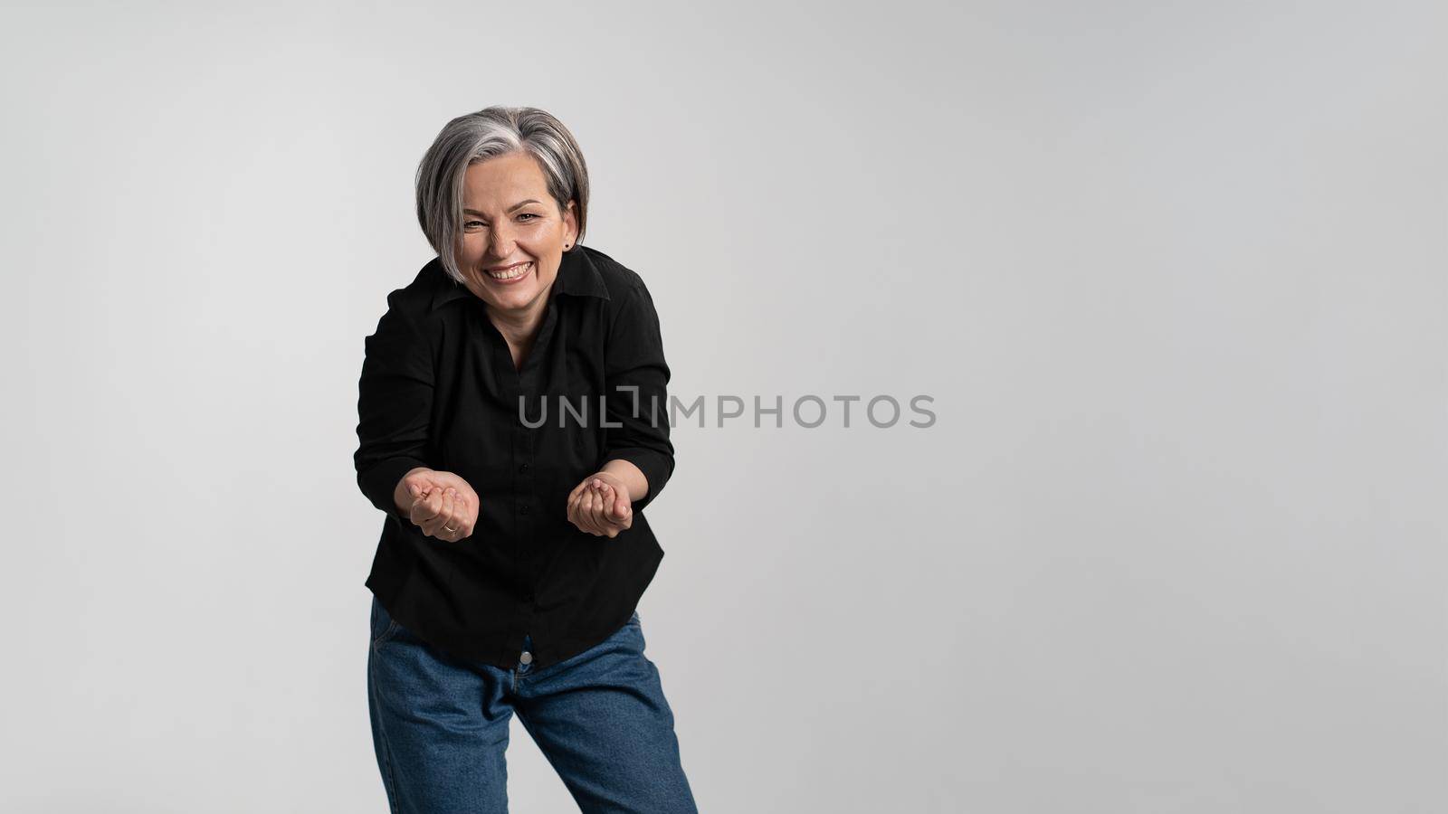 Happy to see her grand kids bowed and hands stretched forward grey haired mature woman wearing black shirt isolated on grey background. Human emotions, facial expression concept.
