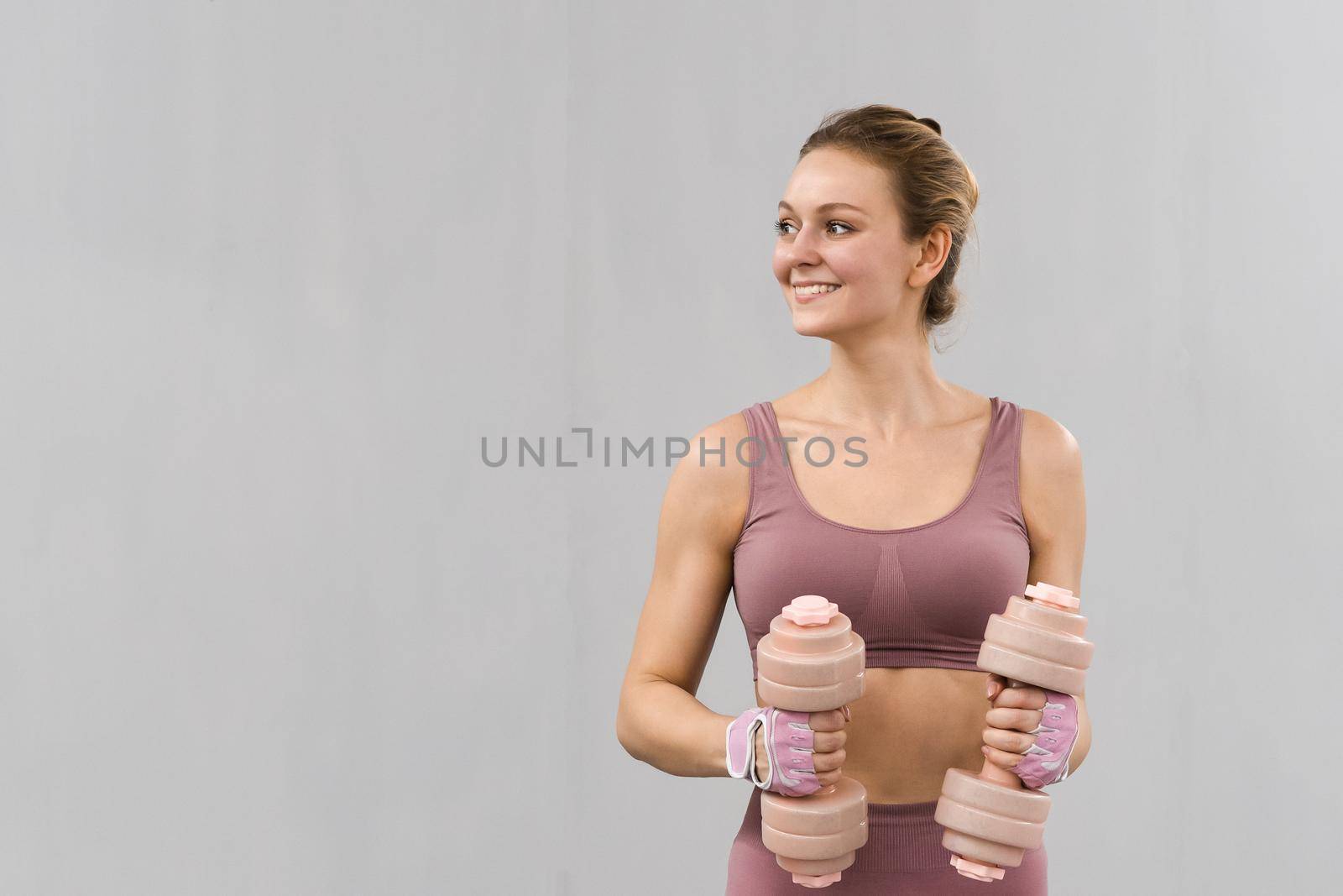 Working out with dumbbells young girl in tight pink outfit. Beautiful fitness girl training legs and lifting weights. Girl doing sports in a loft interior studio. Healthy lifestyle concept.