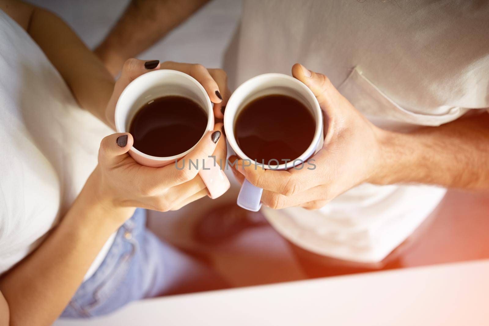 Top view. Two hands with cups of coffee, holding by young couple standing at the morning on the kitchen.