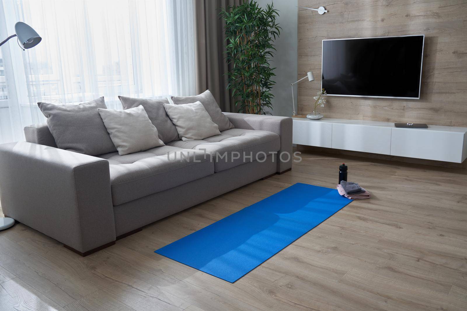 Yoga mat on the floor near couch in modern living room with no people. Healthy lifestyle and fitness concept by Mariakray