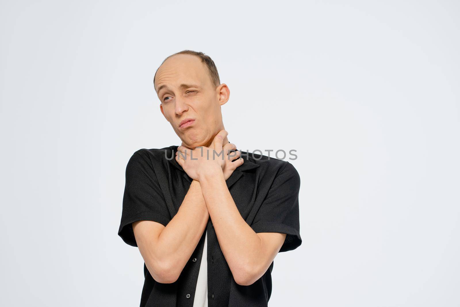 Choking himself or playfully trying to show the interlocutor enough young bald man wearing black shirt with white t-shirt underneath. Young adult man with hands on his neck on white background by LipikStockMedia