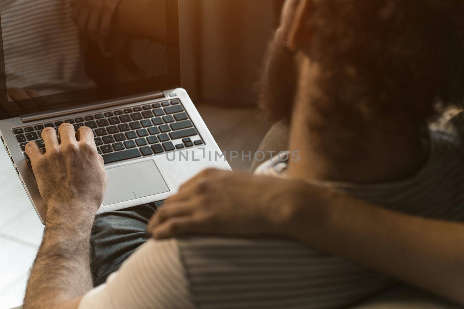 Shot from the back. Working together young couple staying quarantined at home with sitting on the arm chairs. Happy young couple sitting on a chair together using laptop by LipikStockMedia