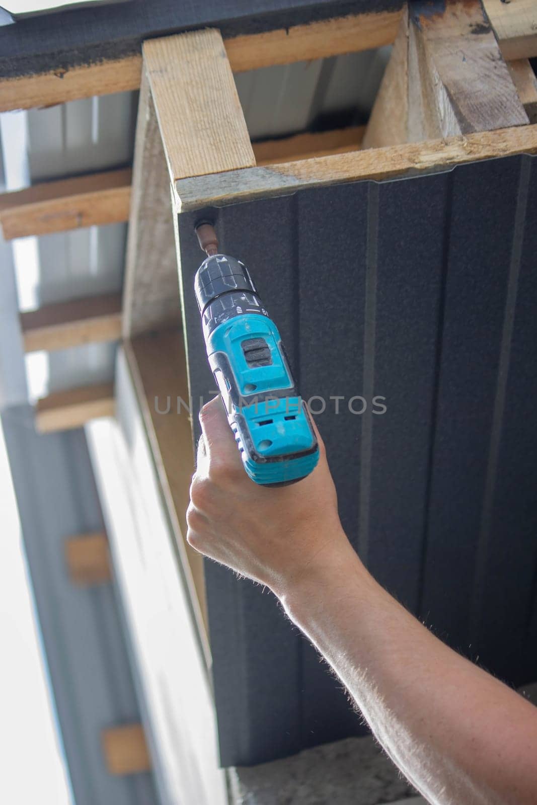 a man repairs the roof, tightens the self-tapping screw with a screwdriver. Selective focus
