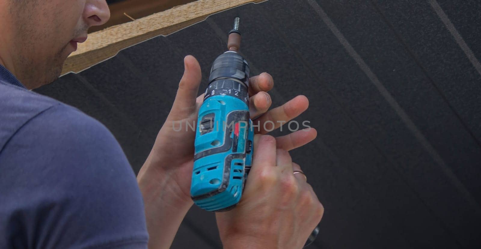 a man repairs the roof, tightens the self-tapping screw with a screwdriver. Selective focus
