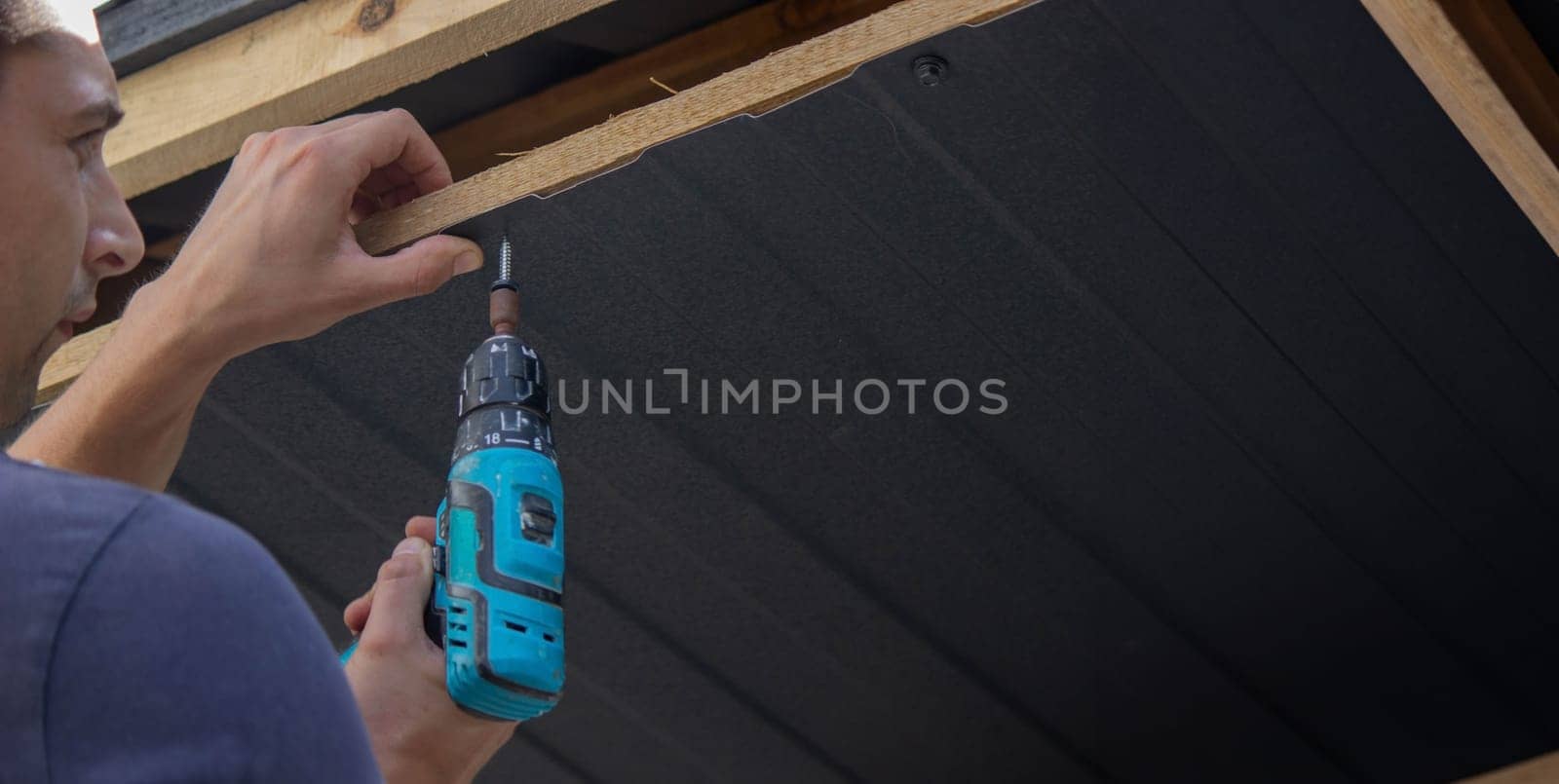 a man repairs the roof, tightens the self-tapping screw with a screwdriver. Selective focus