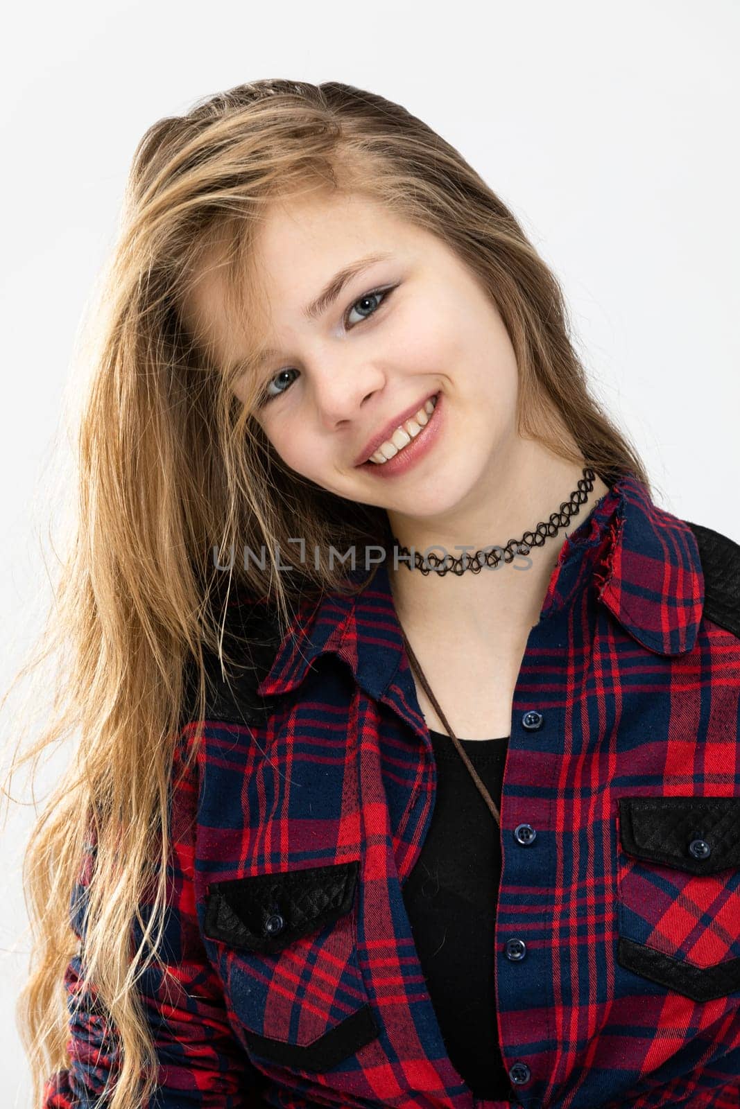 Close-up on the face of a girl who smiles revealing her teeth. A young girl dressed in a checkered shirt. The girl has long hair pulled to the side and tilts her head slightly.