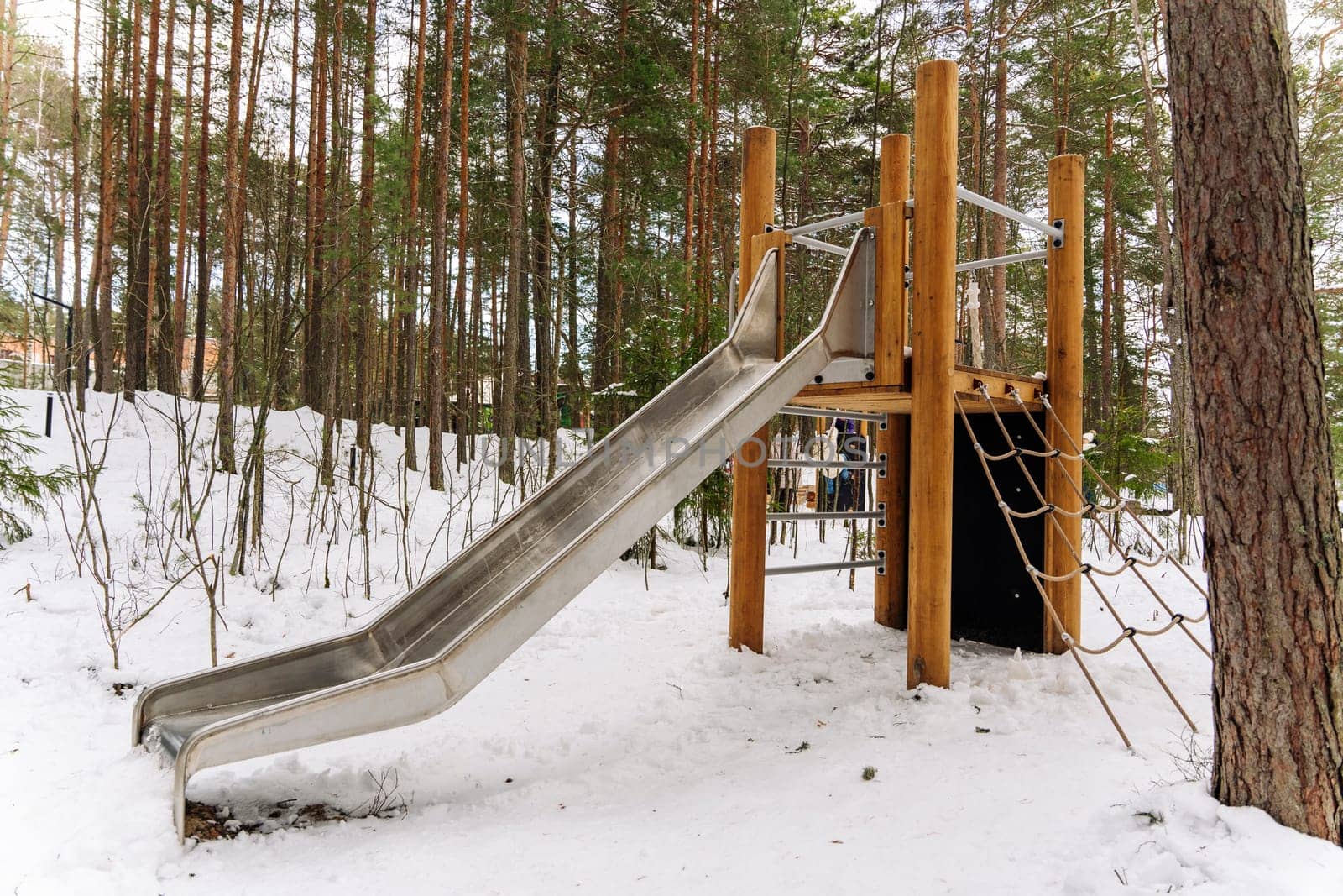 An empty children's slide in a winter amusement park among the pines. Playground in the city park. Walking with children in the fresh air