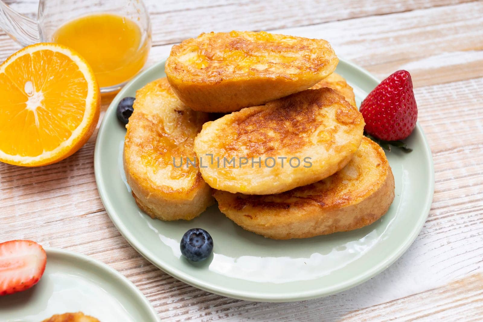Torrijas, Spanish Style French Toast Served With Orange Topping, Glaze, Fresh Blueberries, Strawberry On Green Plate, Wooden Table. A Half Of Orange. Spanish Dessert. Horizontal plane.