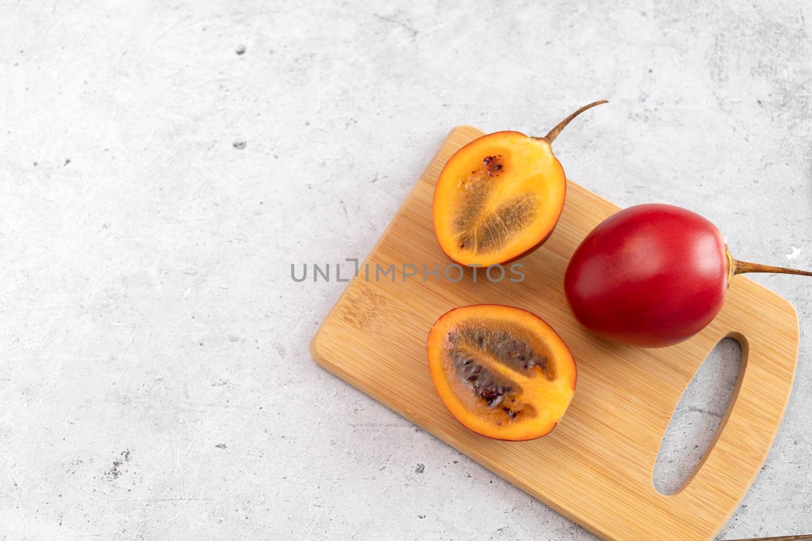 Fresh Exotic Fruit Tamarillo Sliced On Wooded Cutting Board On Table. Egg-shaped Edible Fruit Known As Tree Tomato, Plant Family Solanaceae, Solanum Betaceum. Flatly, copy space. Horizontal Plane.