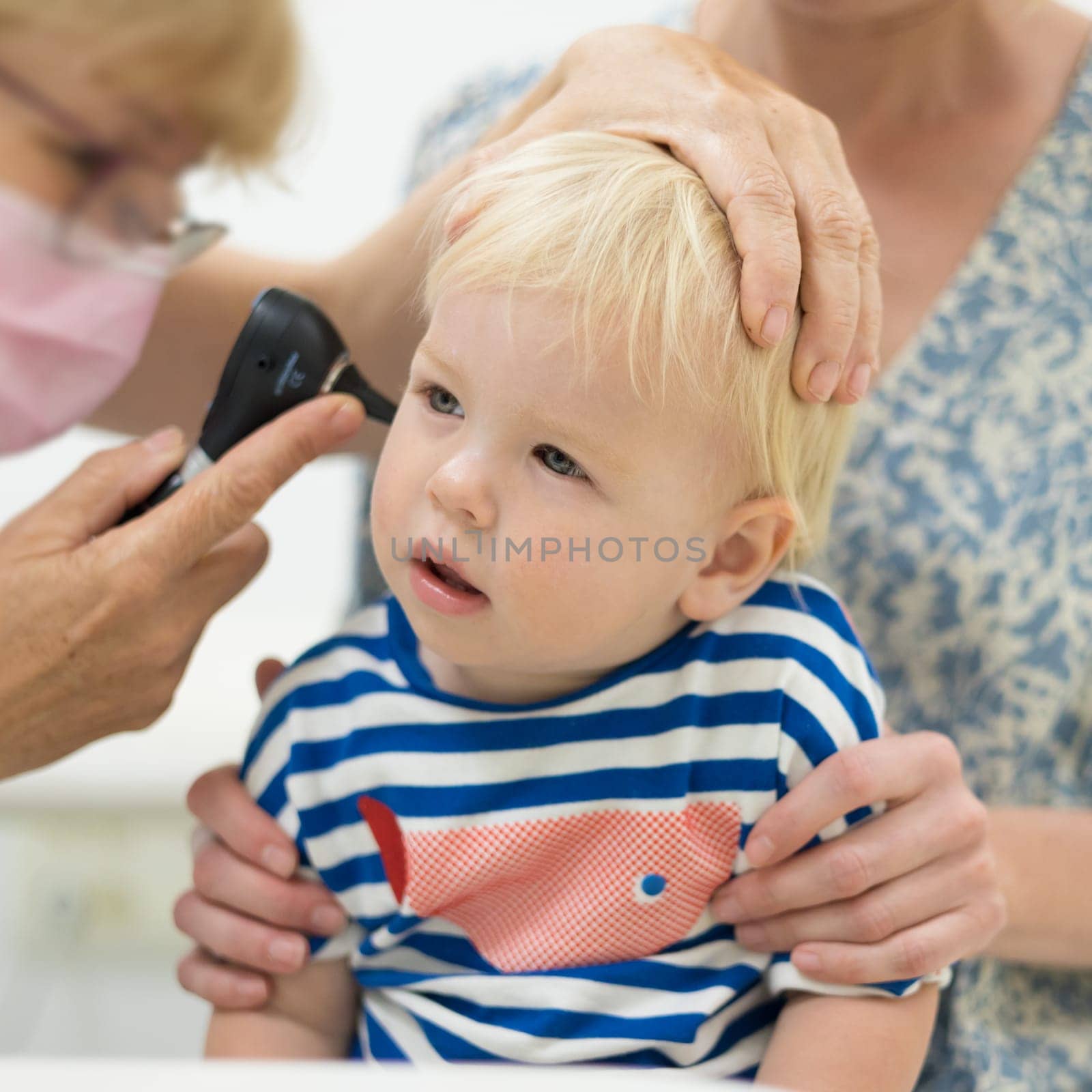 Infant baby boy child being examined by his pediatrician doctor during a standard medical checkup in presence and comfort of his mother. National public health and childs care care koncept