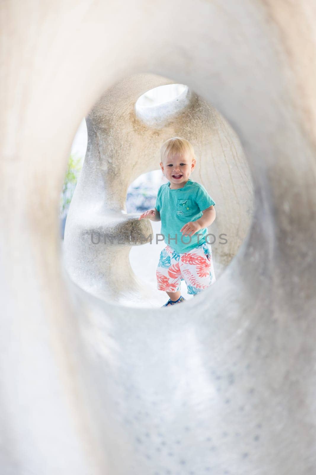 Child playing on outdoor playground. Toddler plays on school or kindergarten yard. Active kid on stone sculpured slide. Healthy summer activity for children. Little boy climbing outdoors