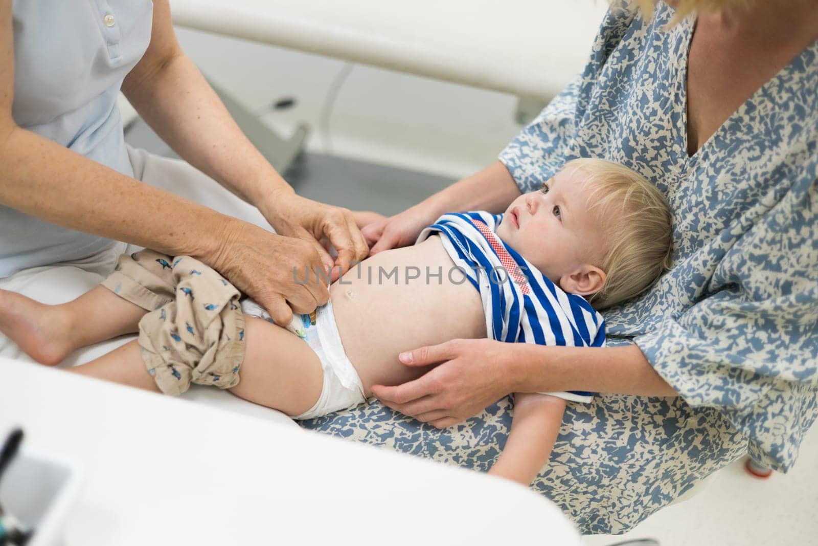 Infant baby boy child being examined by his pediatrician doctor during a standard medical checkup in presence and comfort of his mother. National public health and childs care care koncept