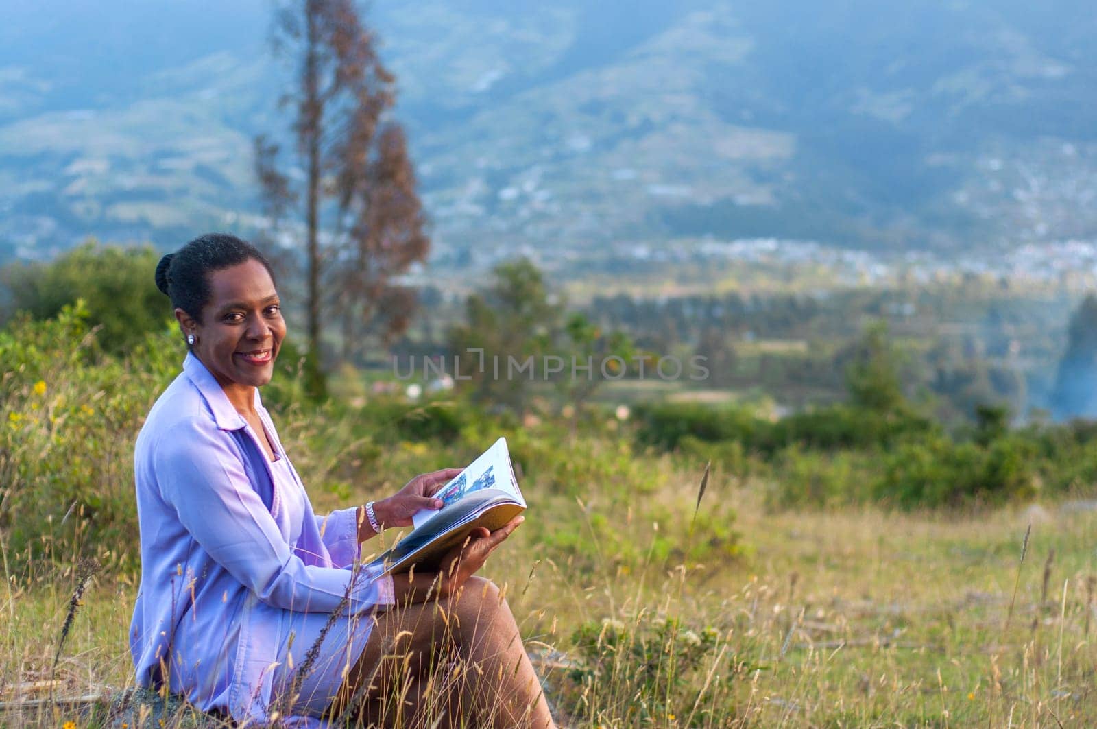 copyspace of elegant african american lady sitting outdoors happy reading a book and smiling at camera. High quality photo