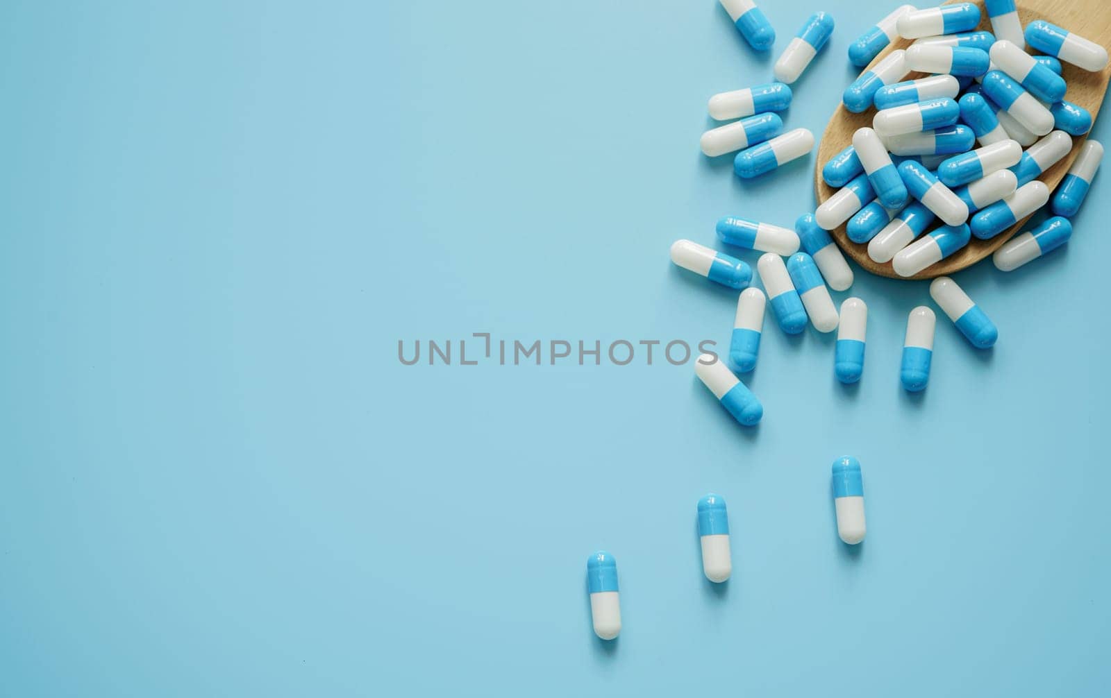 Blue and white antibiotic capsule pill and wooden spoon on blue background. Pills frame with space. Antibiotic drugs. Pharmaceutical industry. Pharmacology. Healthcare and medical care concept.                            