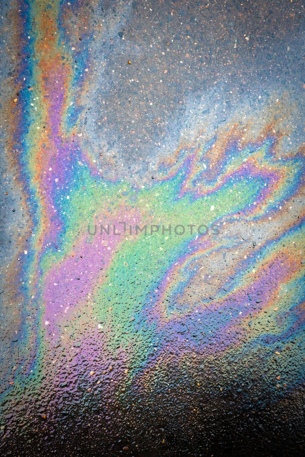 Oil stain on the asphalt, rainbow-shaped colored gasoline stains on an asphalt road as a texture or background. Oil spill on dark asphalt, parking lot.