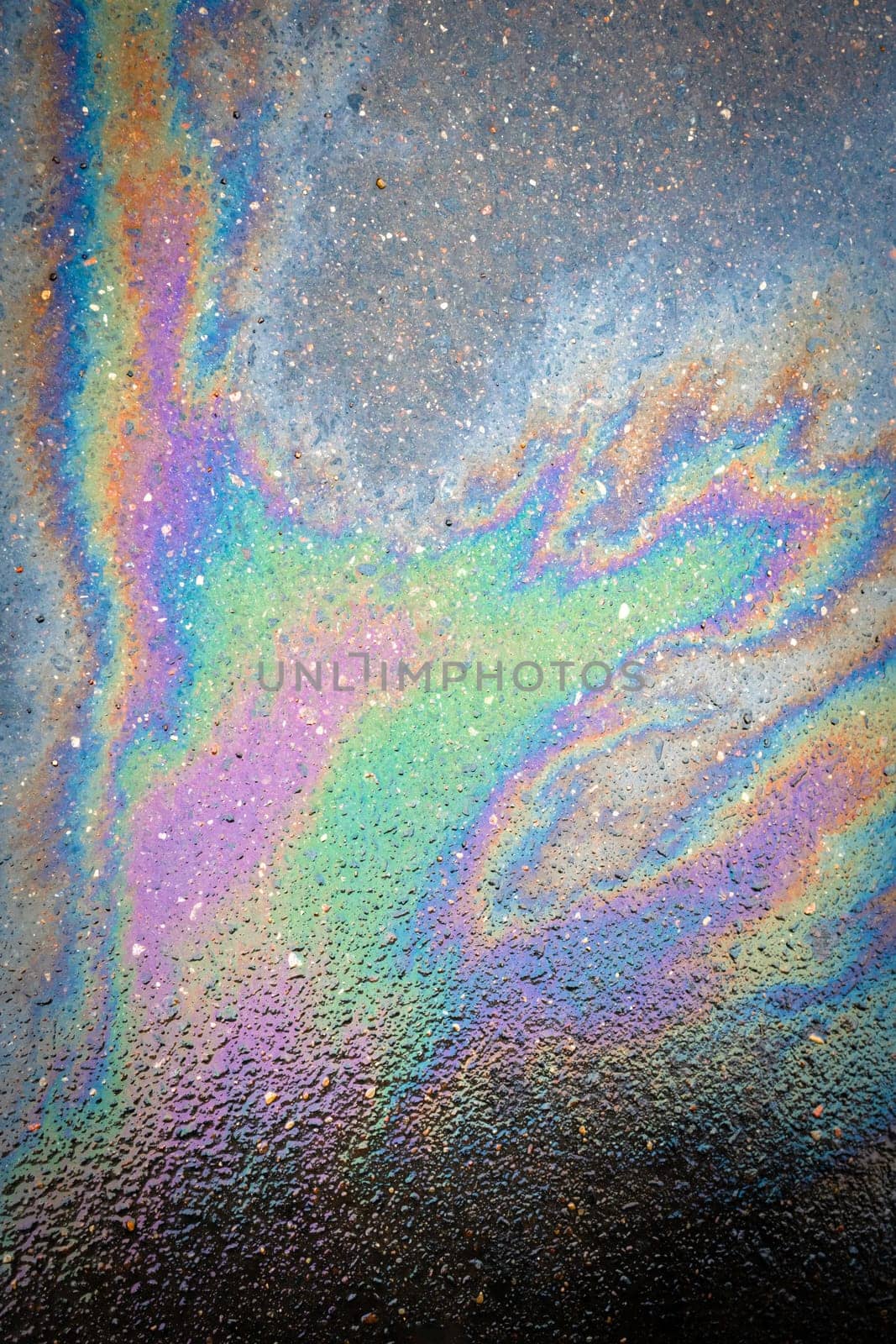 Oil stain on the asphalt, rainbow-shaped colored gasoline stains on an asphalt road as a texture or background. Oil spill on dark asphalt, parking lot.