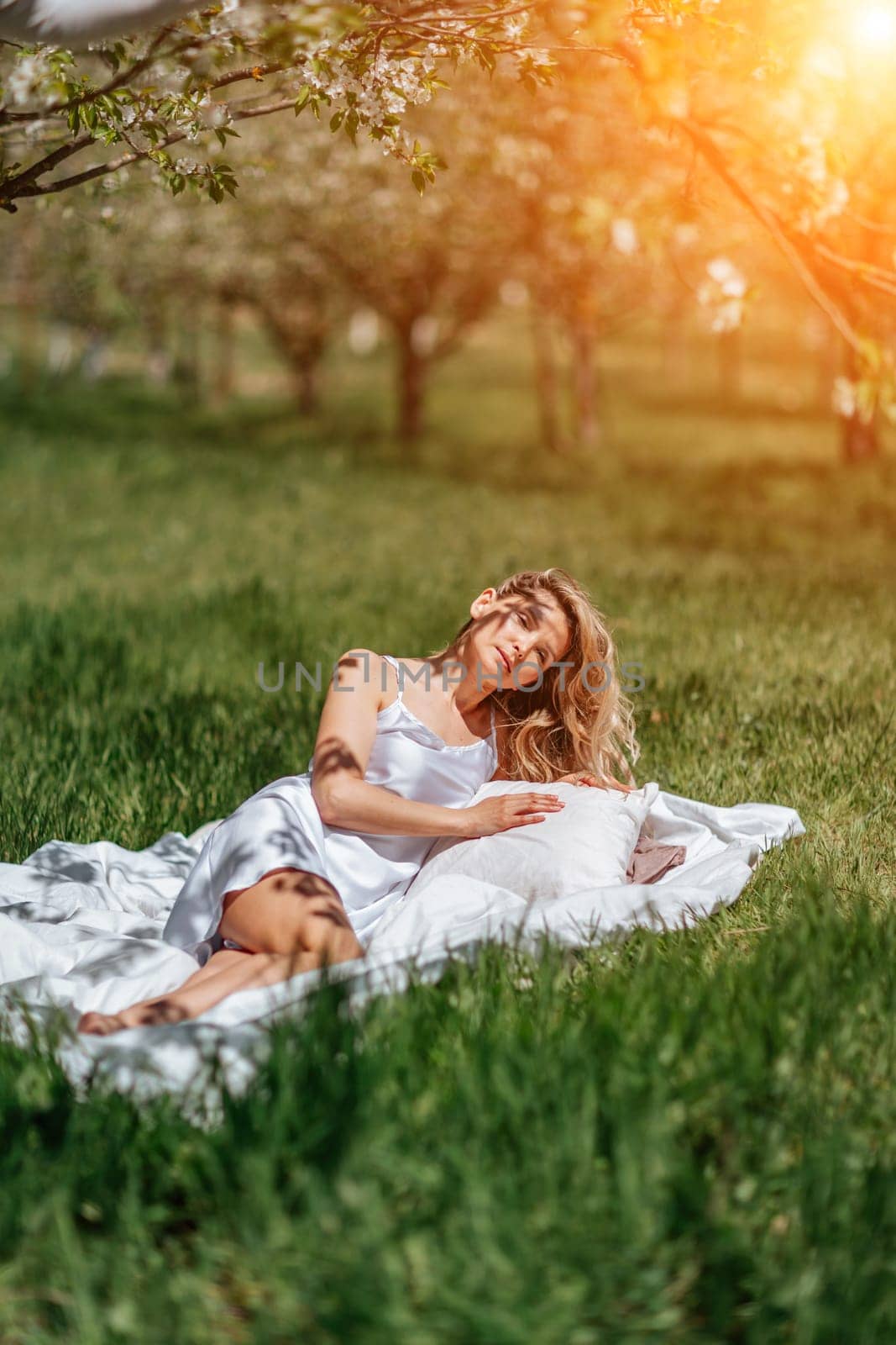 woman garden. she sleeps on a white bed in the fresh spring grass in the garden. Dressed in a blue nightgown. by Matiunina