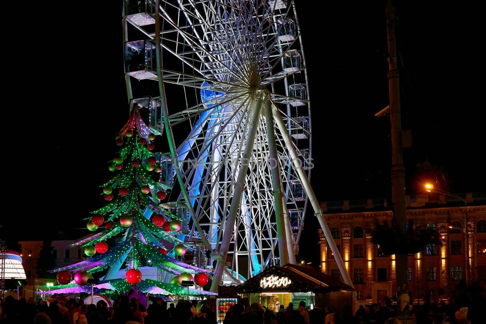 Carousel, Ferris wheel, Christmas tree. Fair on the city evening square by jovani68