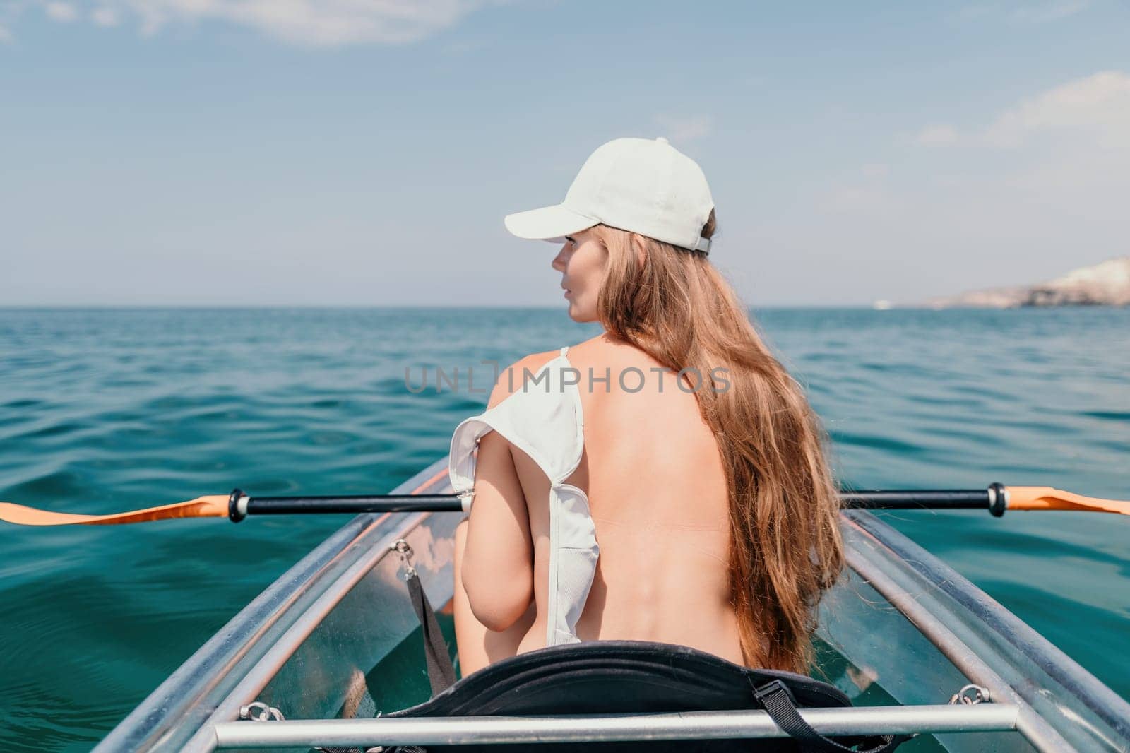 Woman in kayak back view. Happy young woman with long hair floating in transparent kayak on the crystal clear sea. Summer holiday vacation and cheerful female people relaxing having fun on the boat by panophotograph