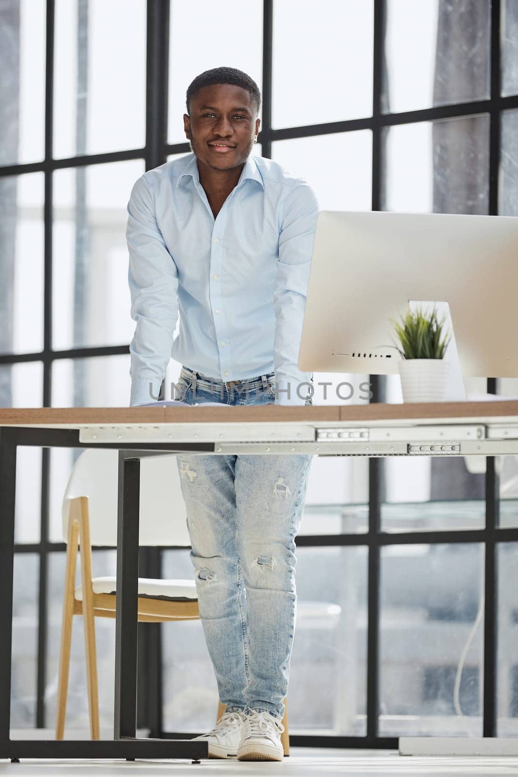 Serious thoughtful millennial businessman standing leaning on desk in home office loft interior