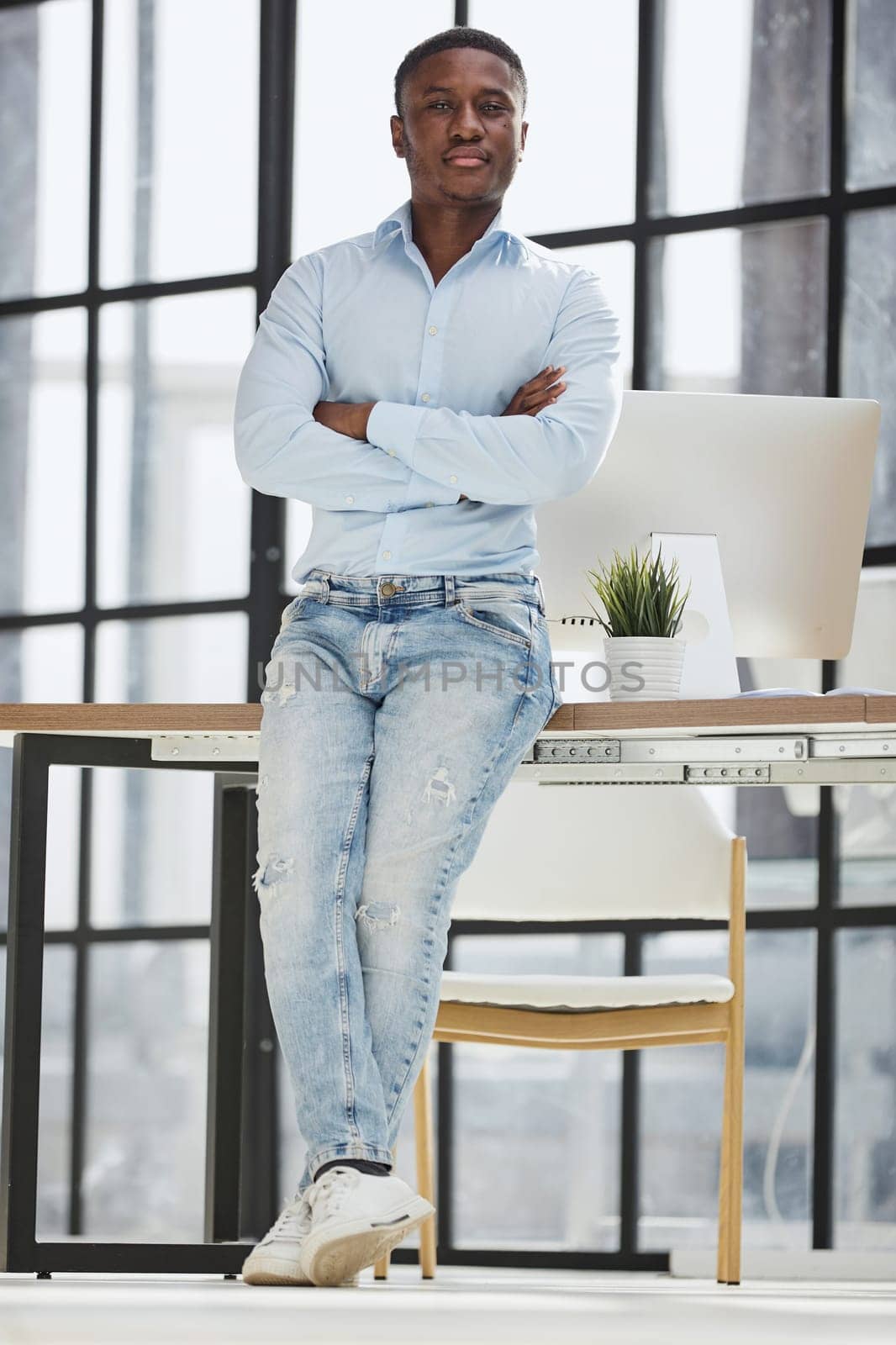 african american man sitting on a table and posing with folded hands in his office