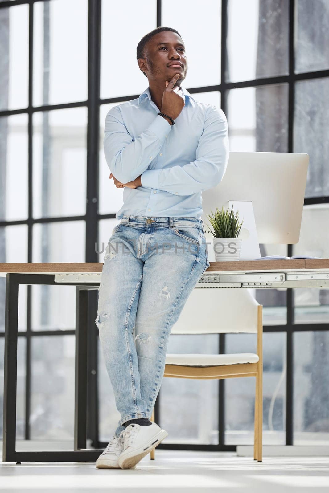 african american man sitting on a table and posing with folded hands in his office