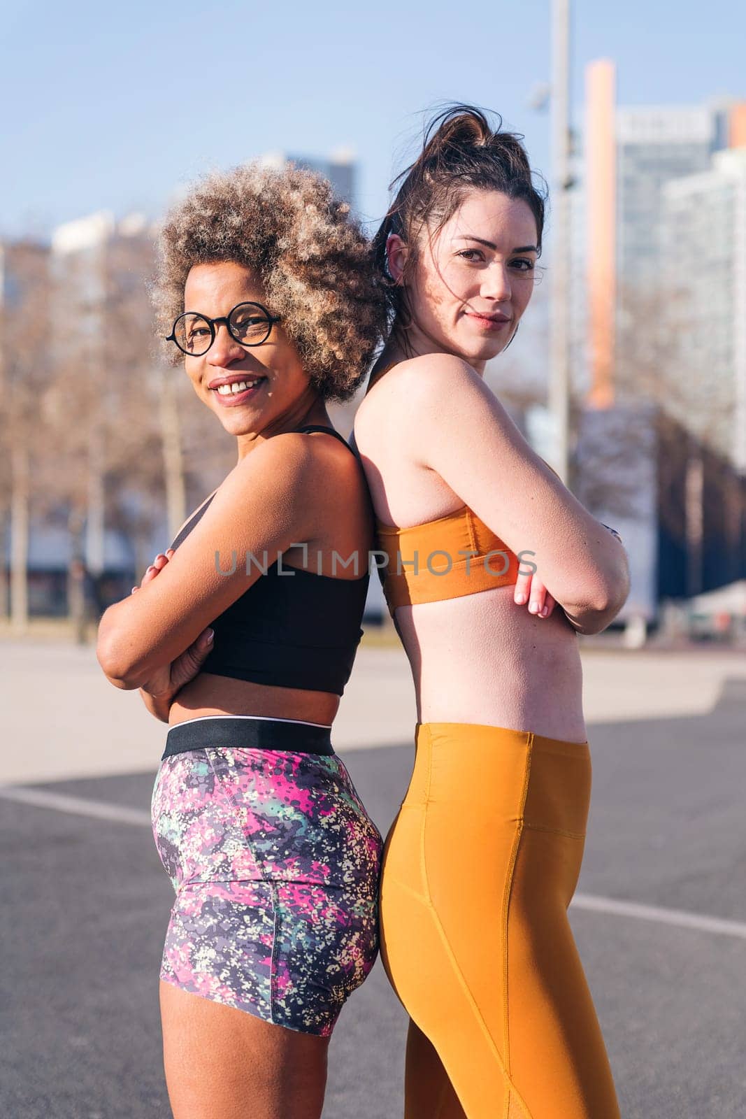 vertical portrait of two female runners standing looking at camera with arms crossed in the city, concept of friendship and sportive lifestyle