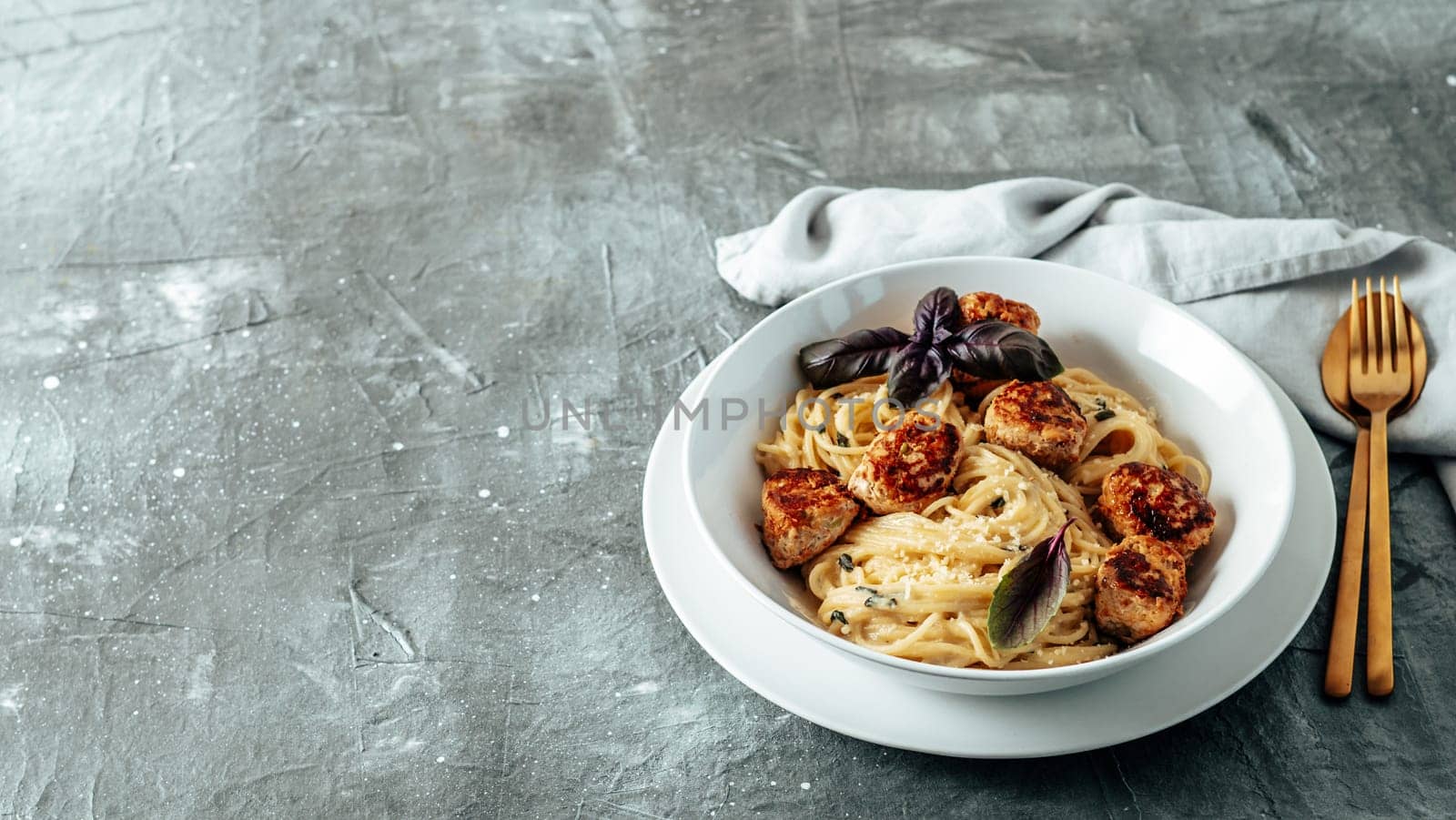 Meatballs Pasta Carbonara in white plate over gray background. Close up view of creamy carbonara pasta with meatballs with copy space left. Comfort food concept