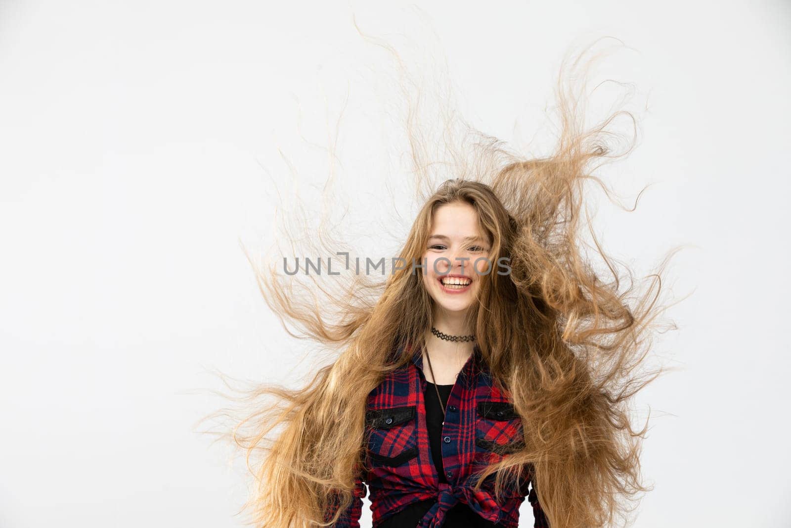 A girl in a checkered shirt tied in a knot laughs. A wind blows from behind and blows the girl's hair away. The long brown hair flies in all directions and tangles.