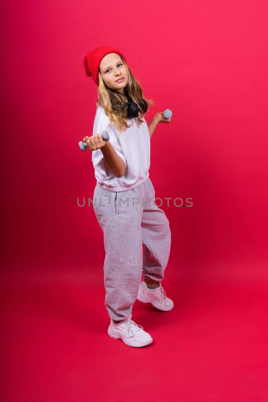 Kid girl doing fitness exercises with dumbbells on red background by Zelenin