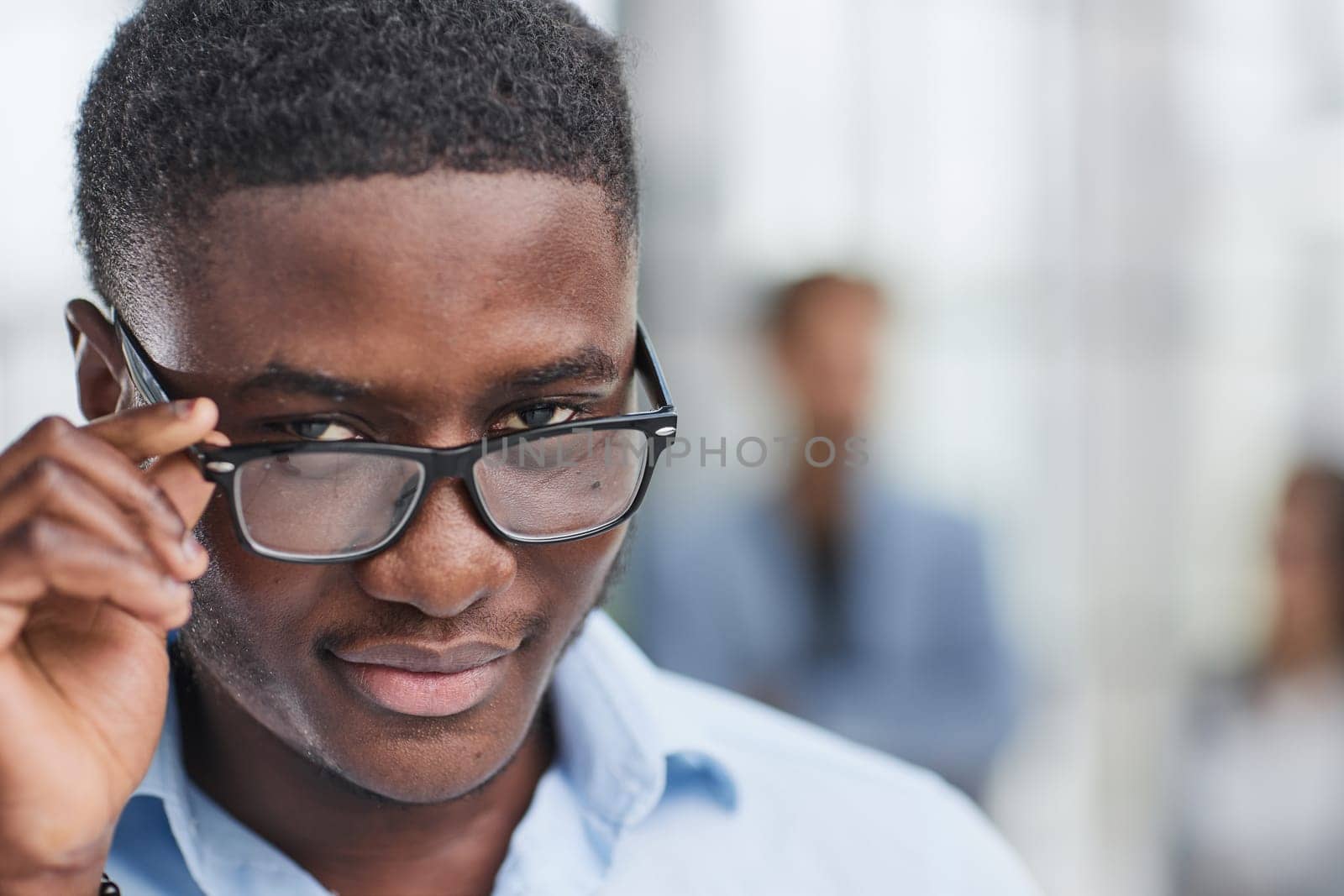 a black man in a blue shirt adjusts his glasses. Against the backdrop of the office