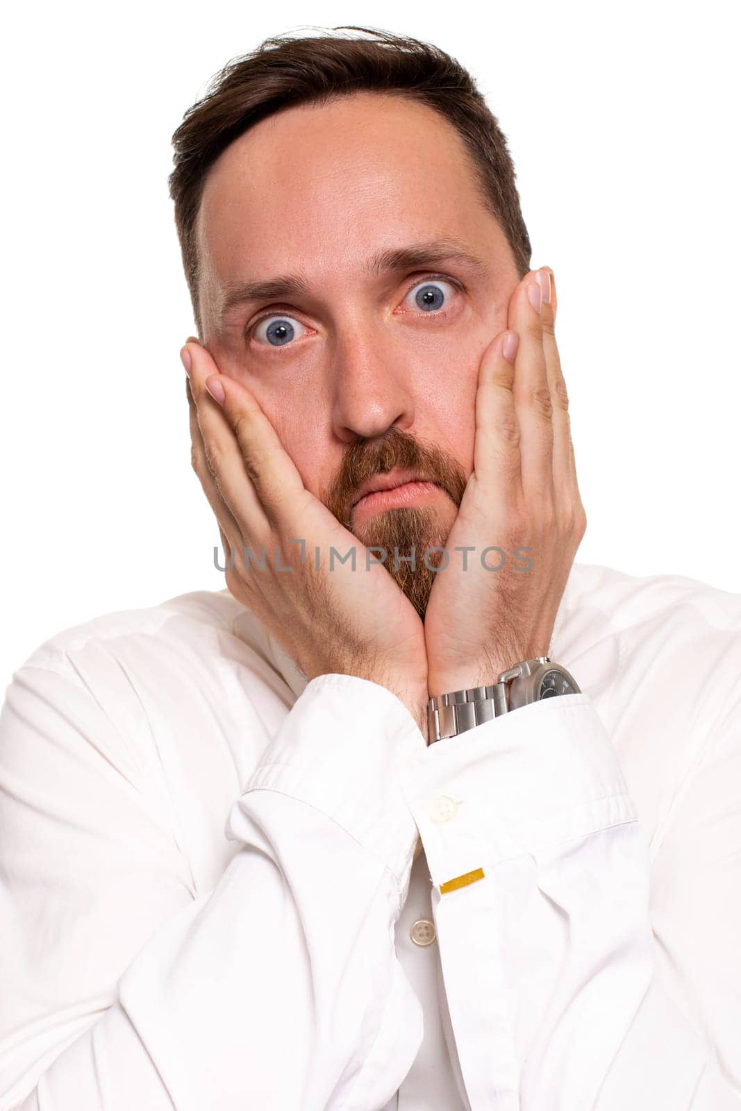 Portrait of bothered handsome young man in white shirt holding palms near cheek. Facial expressions and reaction concept