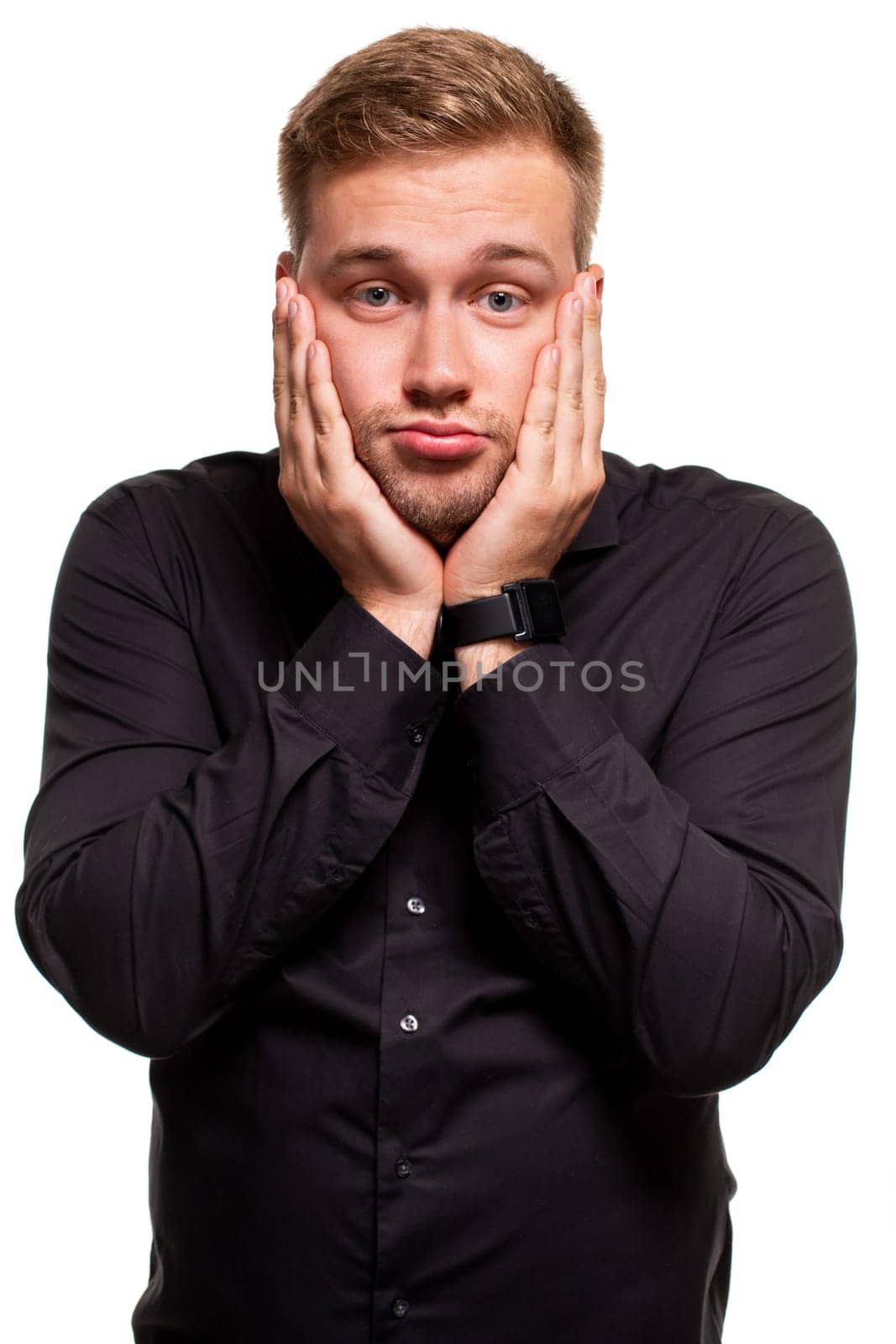 Studio portrait of gloomy european man showing boredom while leaning head on hand and standing over white background. I am not interested in all this stupid rumors.