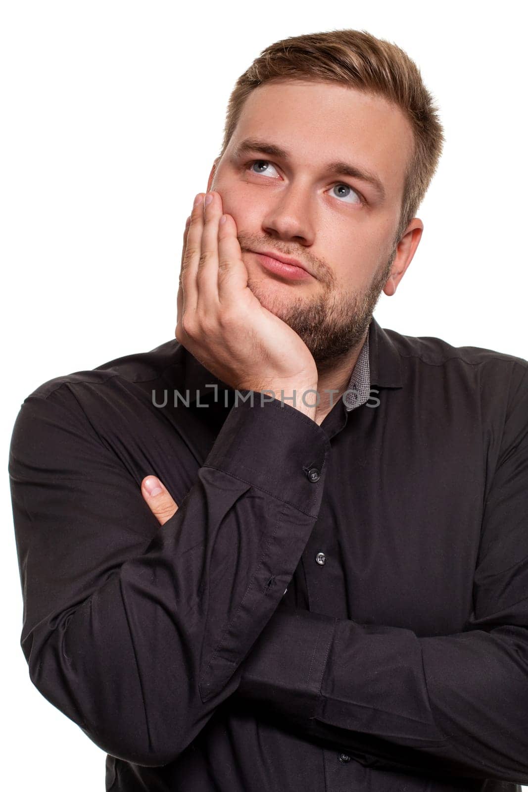 Studio portrait of gloomy european man showing boredom while leaning head on hand and standing over white background. I am not interested in all this stupid rumors.