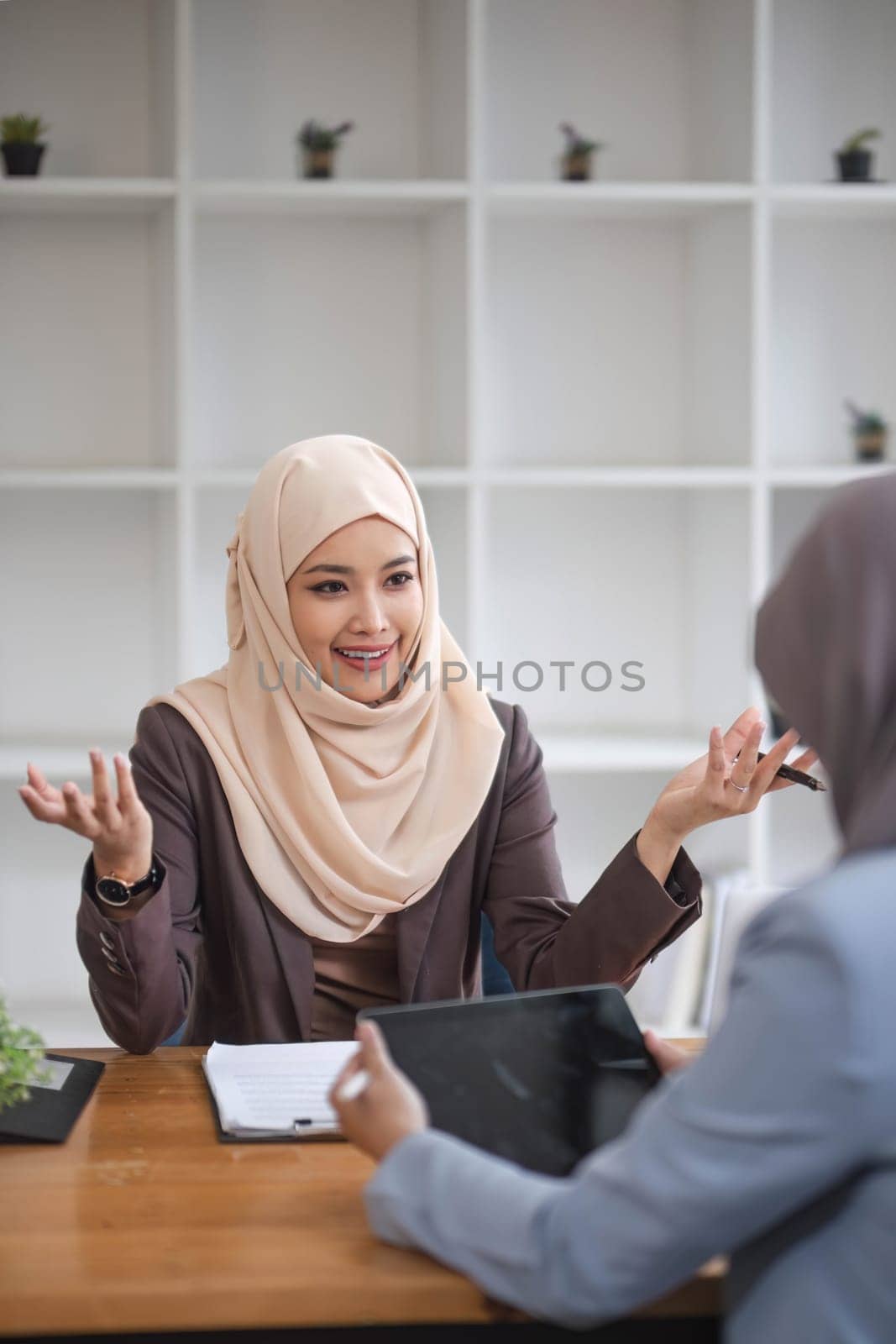 A professional and confident Asian Muslim businesswoman discussing work with her colleague in the office. by wichayada