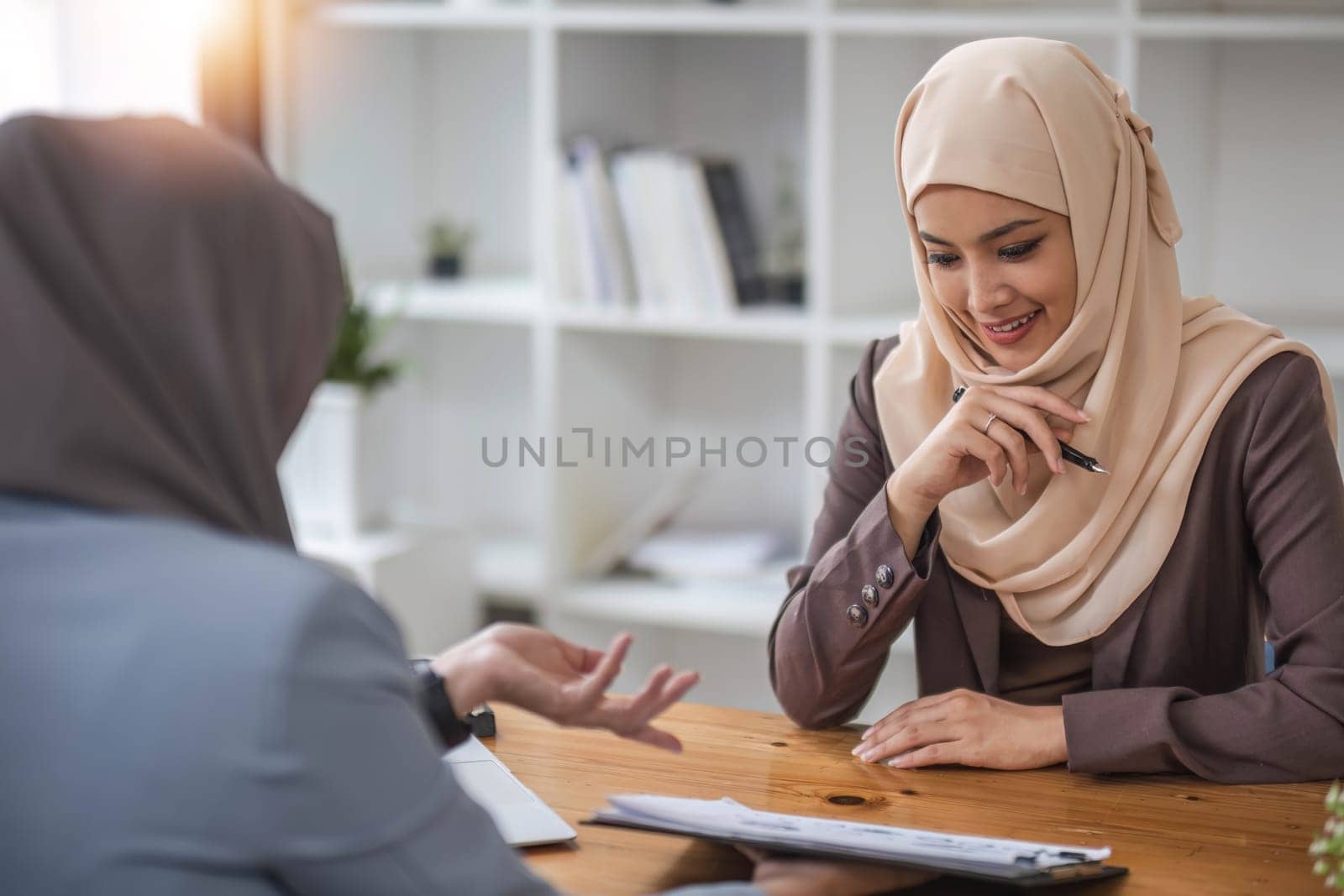 A professional and confident Asian Muslim businesswoman discussing work with her colleague in the office...