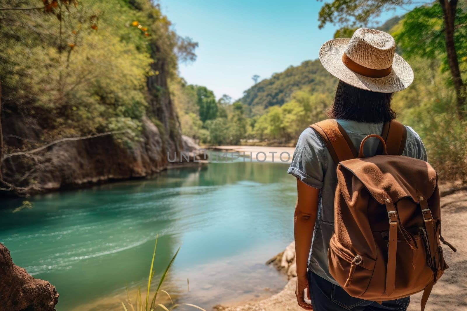 A traveling woman, with backpack and straw hat, gazes at a scenic river in a lush tropical setting.