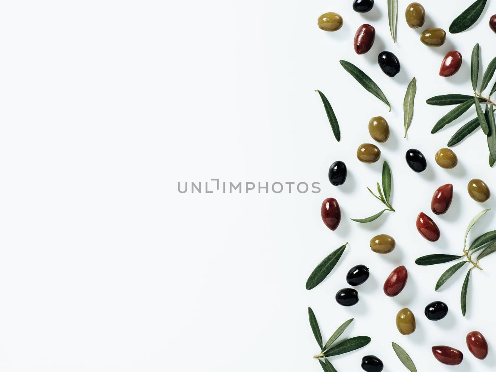 Pattern with green, black and red olives and olives tree leaves and branches on white background. Mix olive tree fruits and branches as background with copy space. Top view or flat lay.